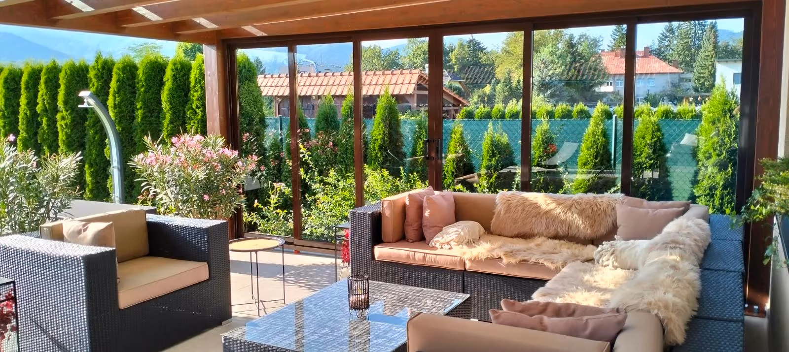 Berendezett Milano fa pergola nagy ülőgarnitúrával egy vörös tetős ház mellett