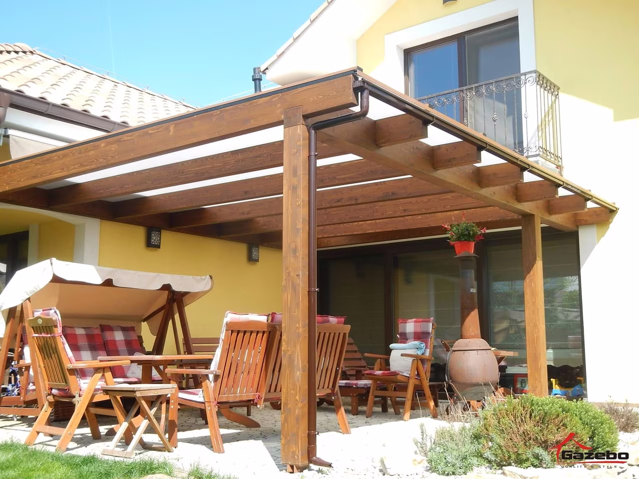 Fenix fa pergola terasz fölött kerti bútorral és hintával sárga ház mellett