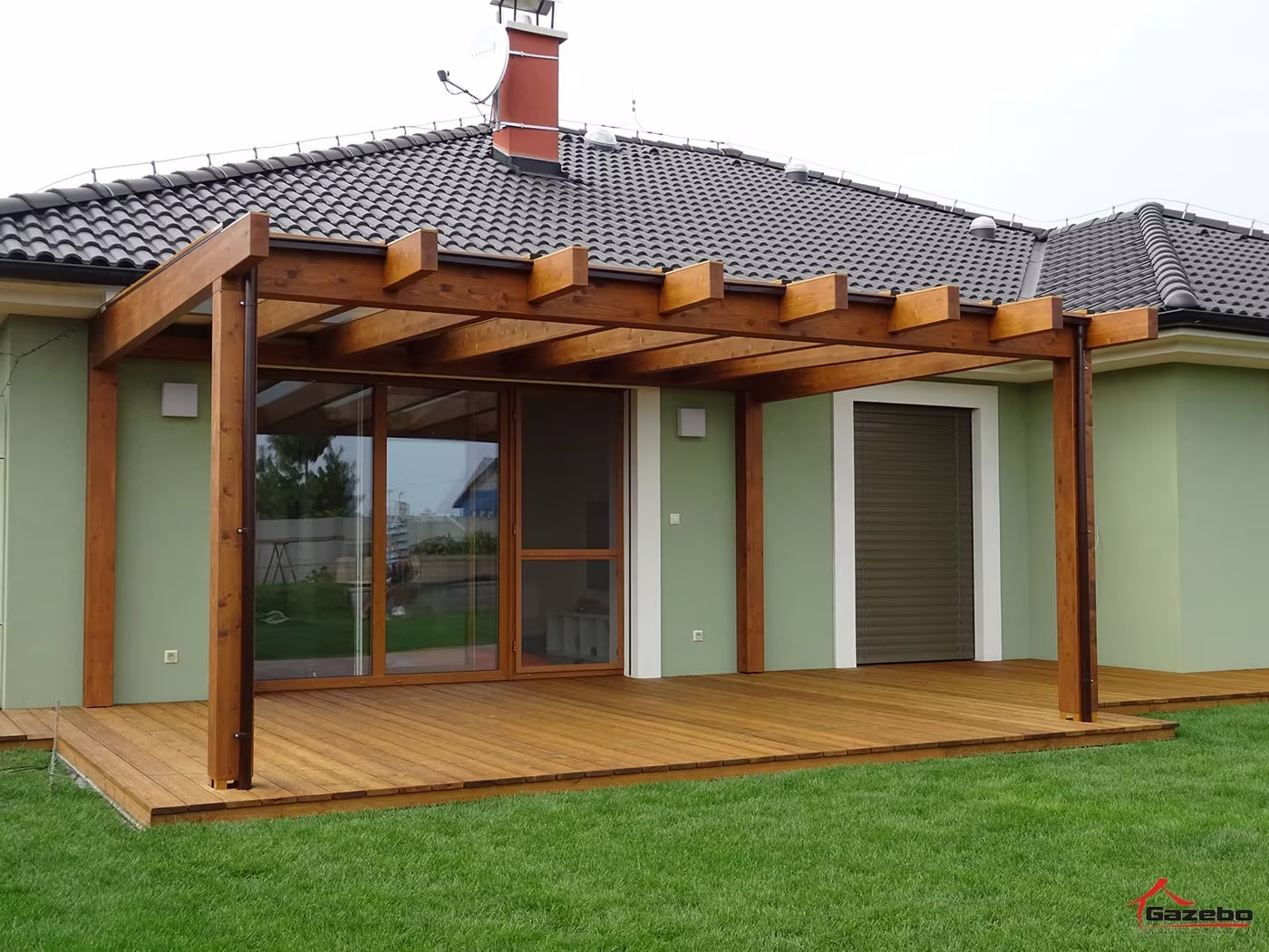 Fenix fa pergola üvegezett ajtós ház mellett fa terasz fölött gyeppel